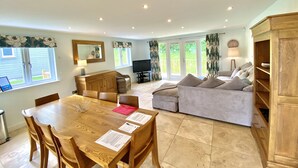A spacious living room with a wooden dining table, a sofa, and a television. - Trewhiddle Villa 2 -  a trewhiddle that sleeps 7 guests  in 4 bedrooms (Saint Austell)