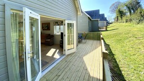 A house with a deck, a sliding glass door leading to an interior room, and a small outdoor seating area. - Trewhiddle Villa 2 -  a trewhiddle that sleeps 7 guests  in 4 bedrooms (Saint Austell)