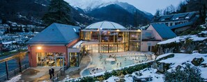 Un hôtel doté d’une piscine intérieure protégée par des parois de verre, entouré de montagnes enneigées.