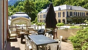 Um pátio externo com mesa e cadeiras, um gazebo e um edifício ao fundo.