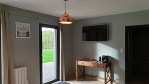 A room with a bed, a desk with a coffee maker, a TV, and a door leading outside. - Cosy Wood House (Laubressel)