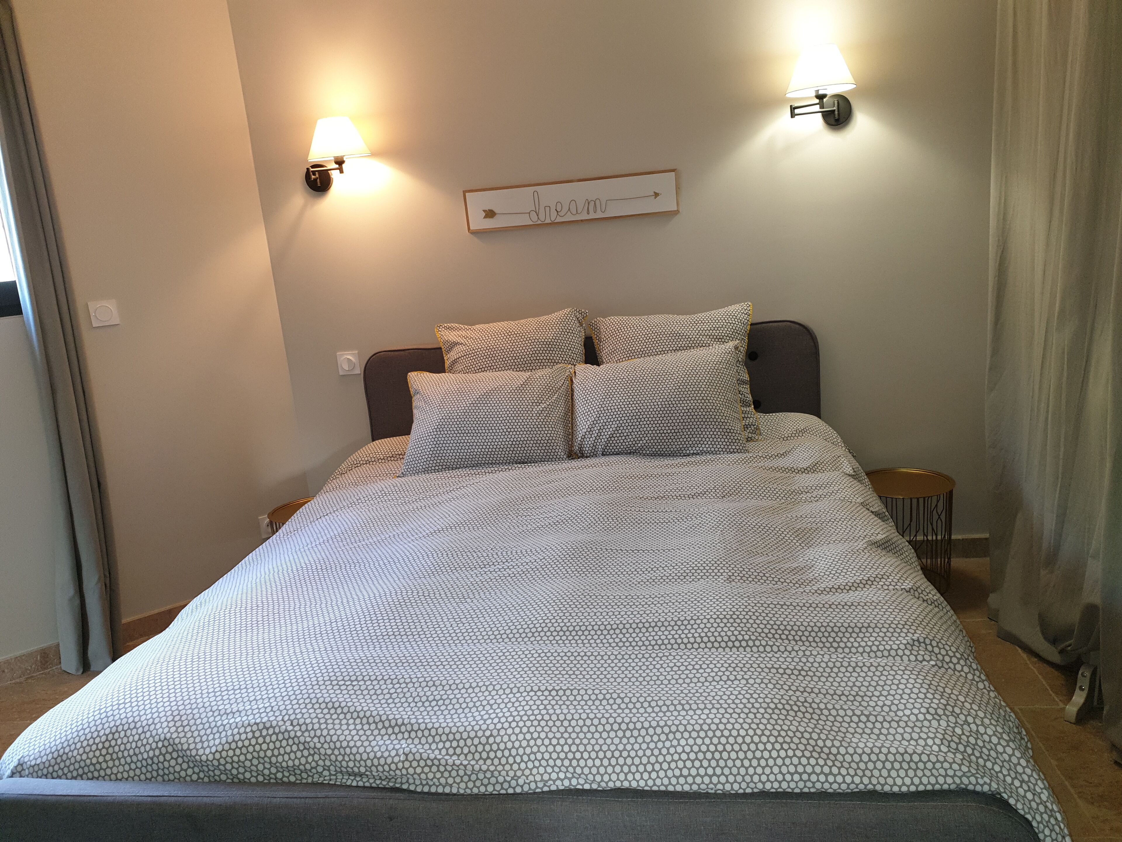 A neatly made bed with a patterned bedspread, two wall-mounted lamps, and a directional sign on the wall.