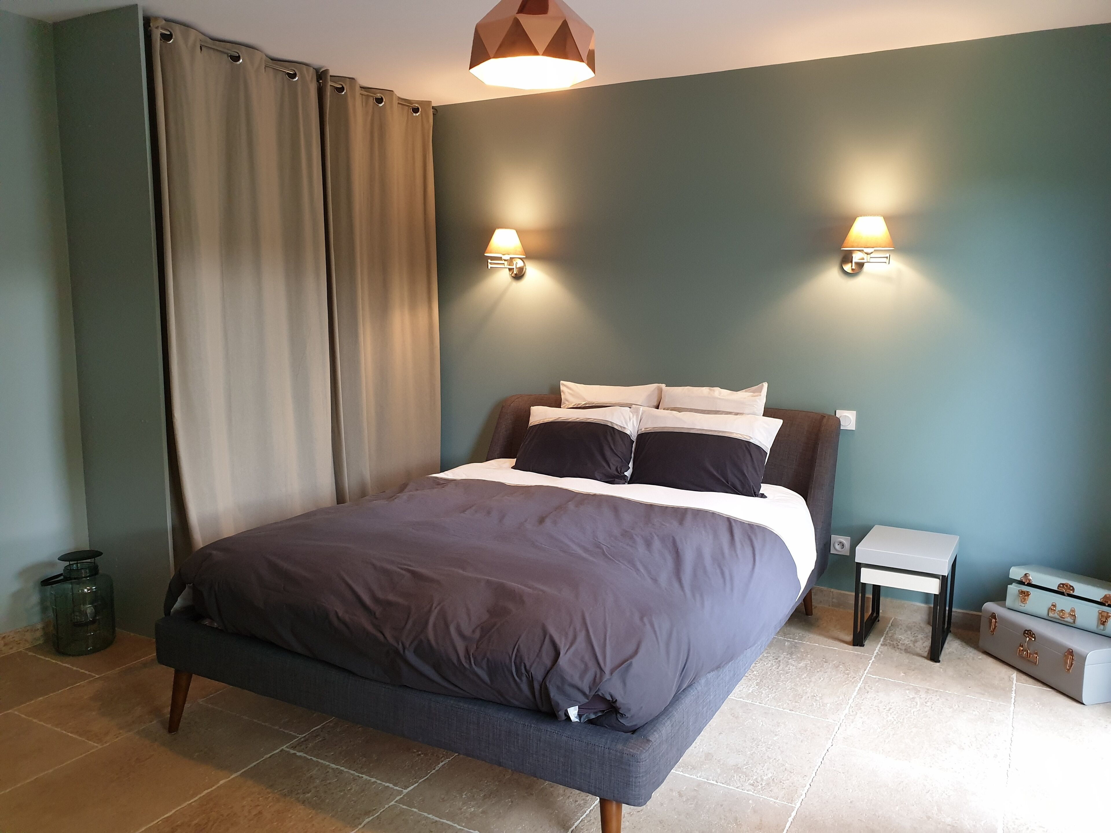 Quarto com cama, duas luminárias de cabeceira, mesa de cabeceira e mala.