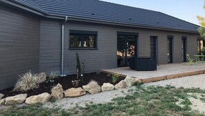 A modern house with a grey exterior, a covered patio, and a garden with rocks and plants. - Cosy Wood House (Laubressel)