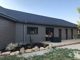 Una casa moderna con fachada gris, un porche cubierto y un jardín con rocas y plantas.