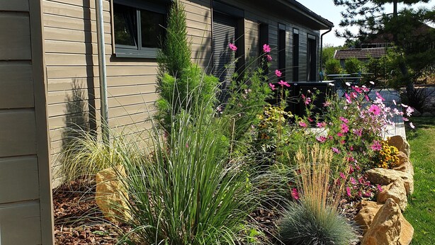 A modern house with a landscaped garden featuring various plants and rocks. - Cosy Wood House (Laubressel)