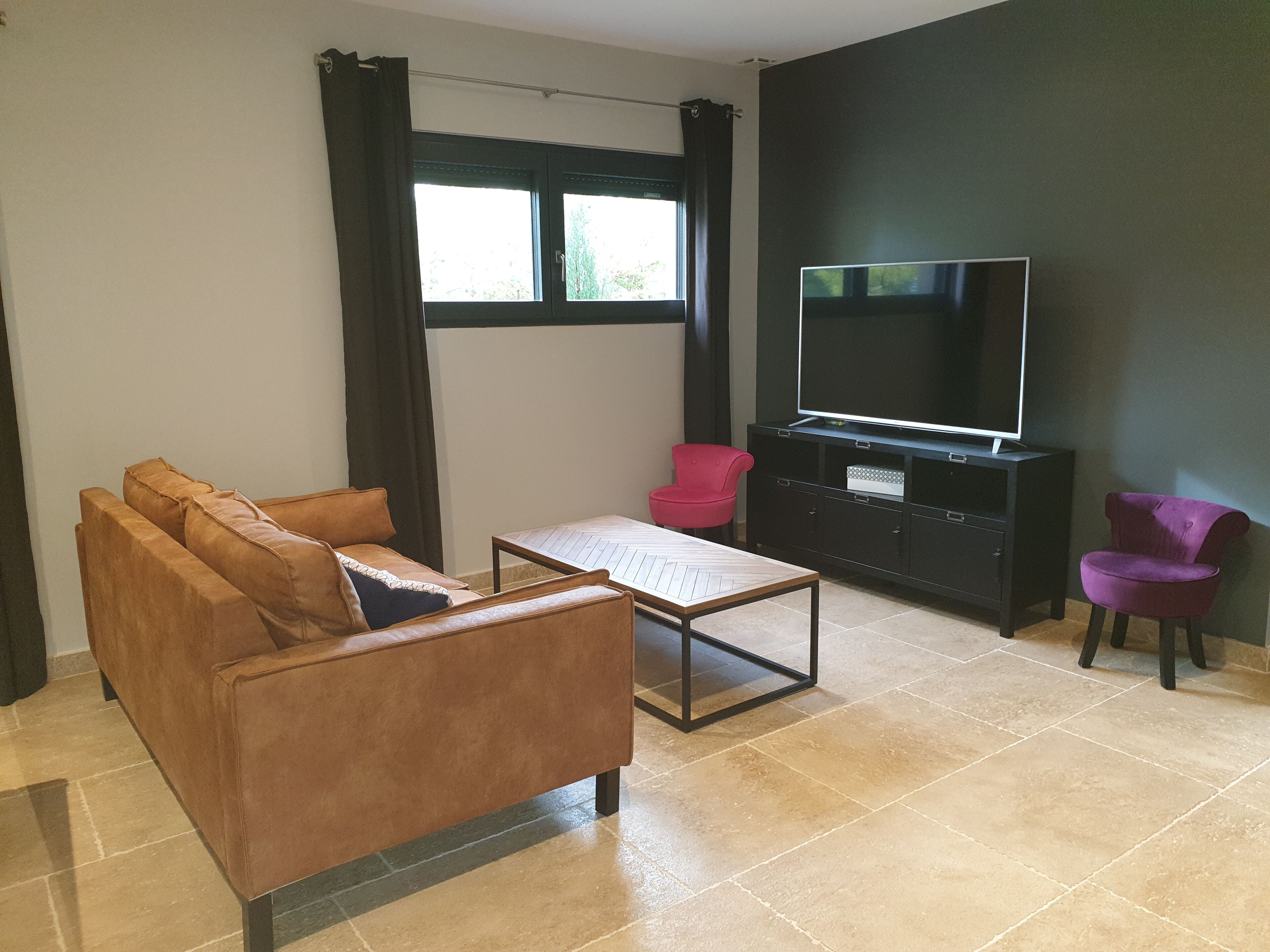 A living room with a brown sofa, a red chair, a black entertainment unit, and a large TV.