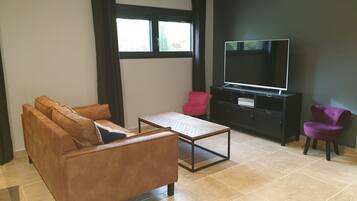 A living room with a brown sofa, a red chair, a black entertainment unit, and a large TV.
