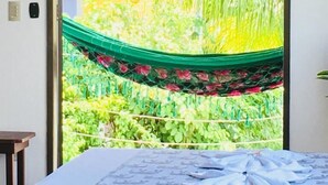 Une chambre avec un lit, un hamac et une vue sur la verdure environnante.