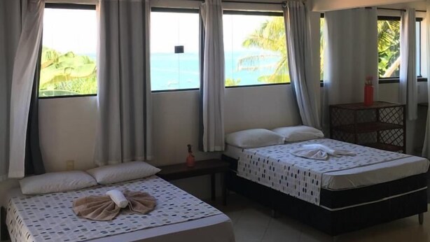 Une chambre avec deux lits, un ventilateur et vue sur la mer.