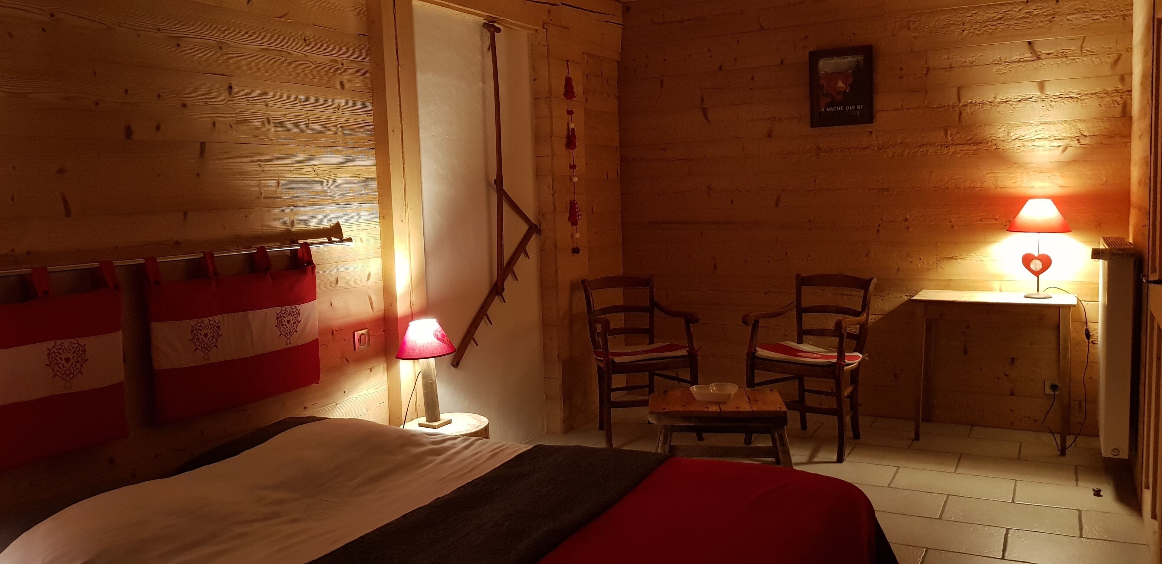 Une pièce en bois avec un lit, deux chaises, une petite table et une étagère fixée au mur.