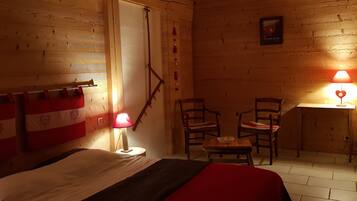 Une pièce en bois avec un lit, deux chaises, une petite table et une étagère fixée au mur.