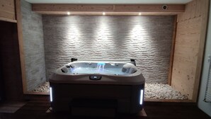 Una bañera de hidromasaje en una habitación con pared de piedra y paneles de madera.