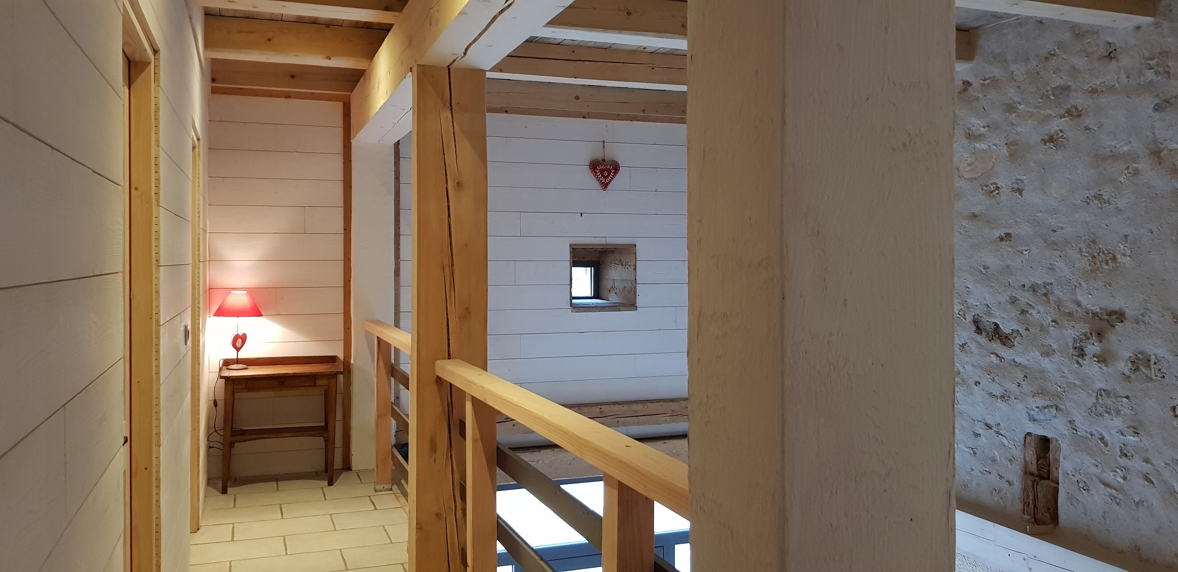 Ein Holzinnenraum mit Schreibtisch und Lampe, einem kleinen Fenster und einer herzförmigen Dekoration an der Wand.