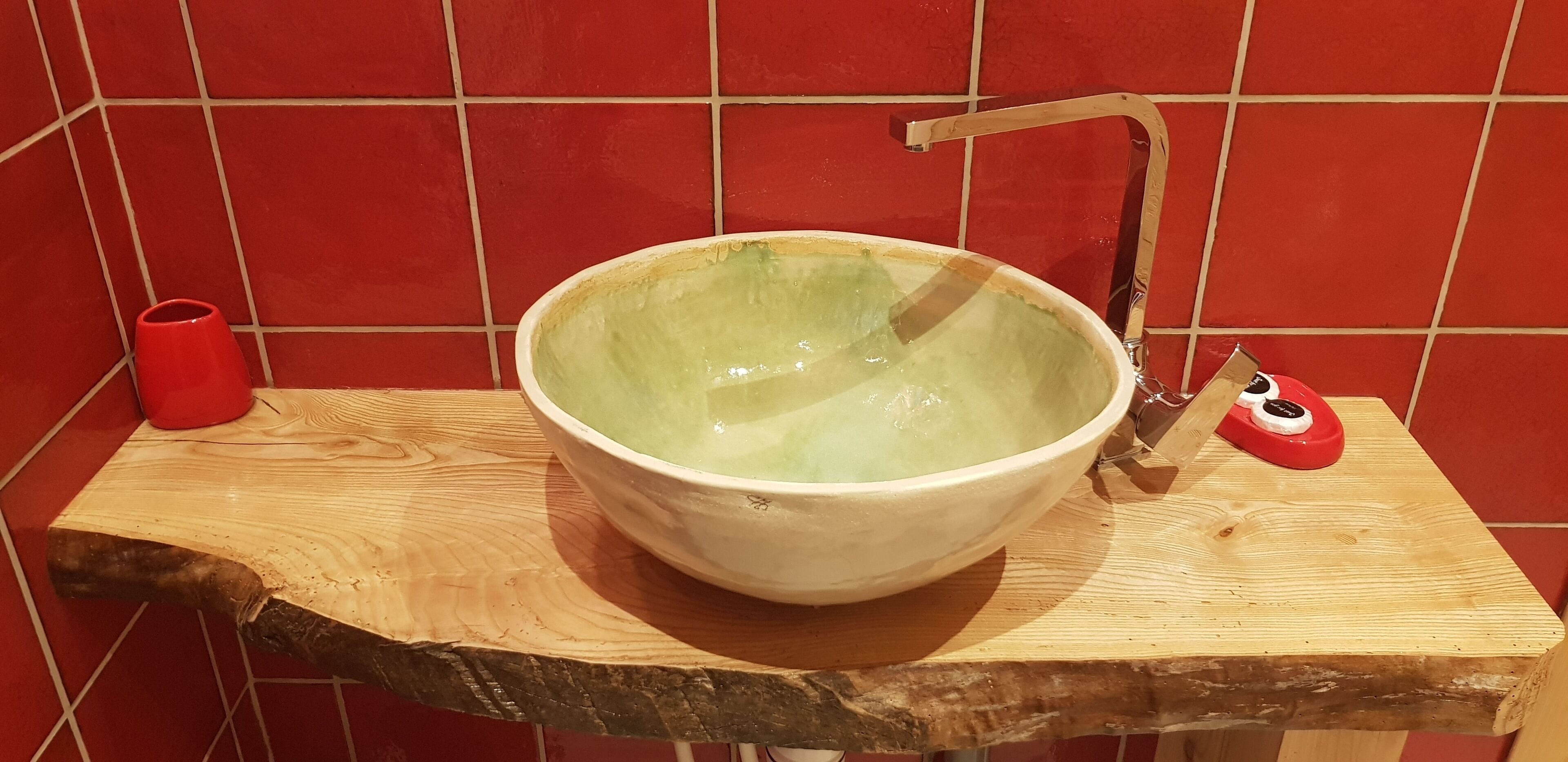 A large ceramic bowl sink with a wooden countertop and a red cup beside it.