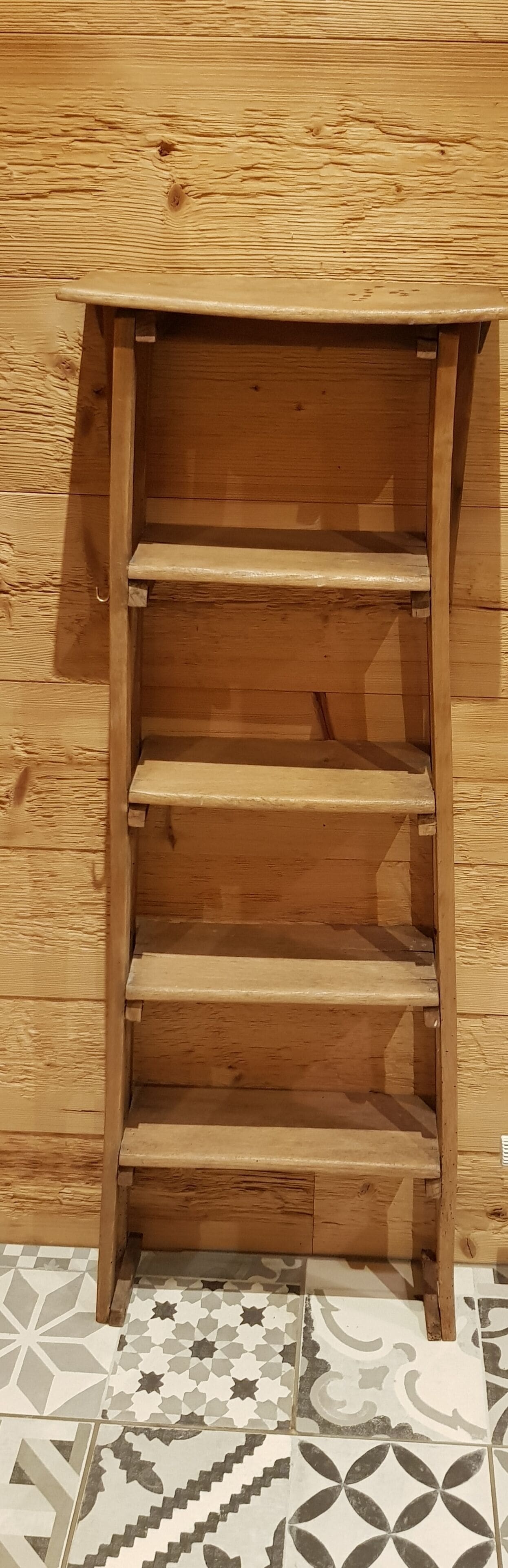 Una estantería de madera contra una pared de madera con suelo de baldosas.
