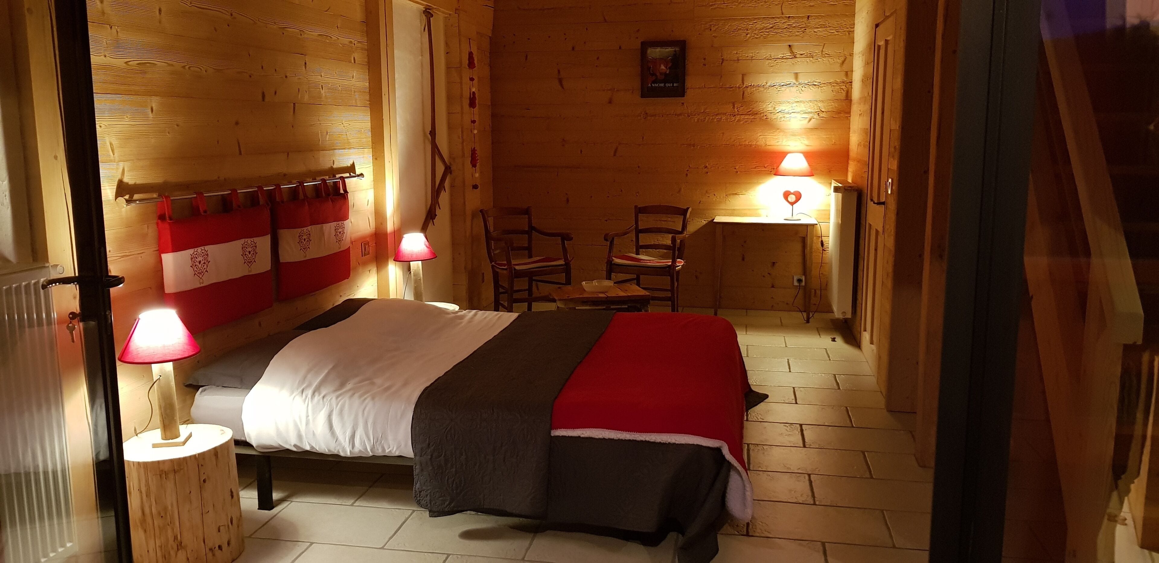 A cozy room with a bed, two chairs, a small table, and a wall-mounted shelf.