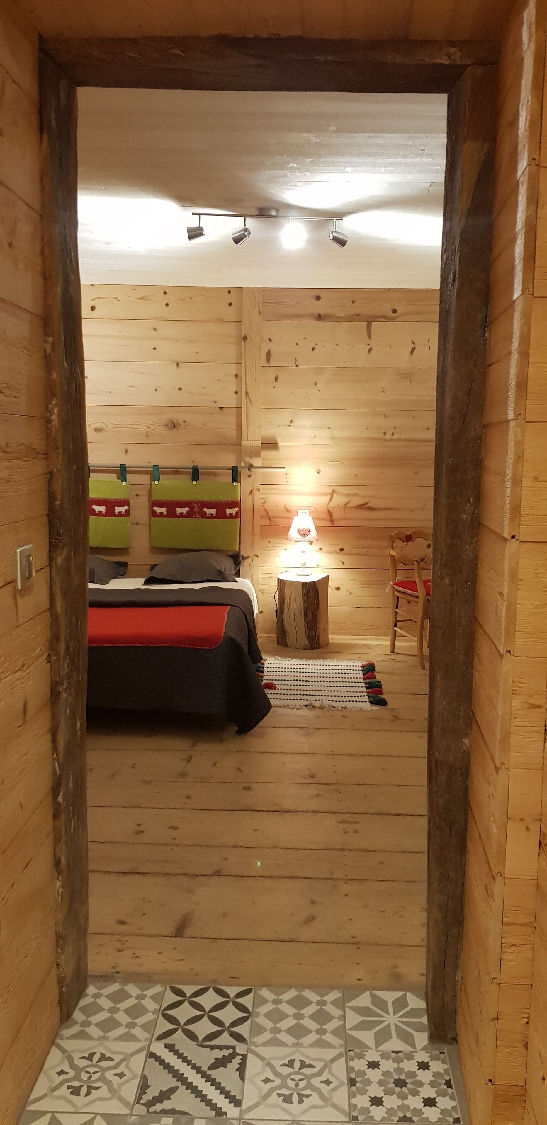 Een houten kamer met een bed, een tafeltje met een lamp en een stoel.