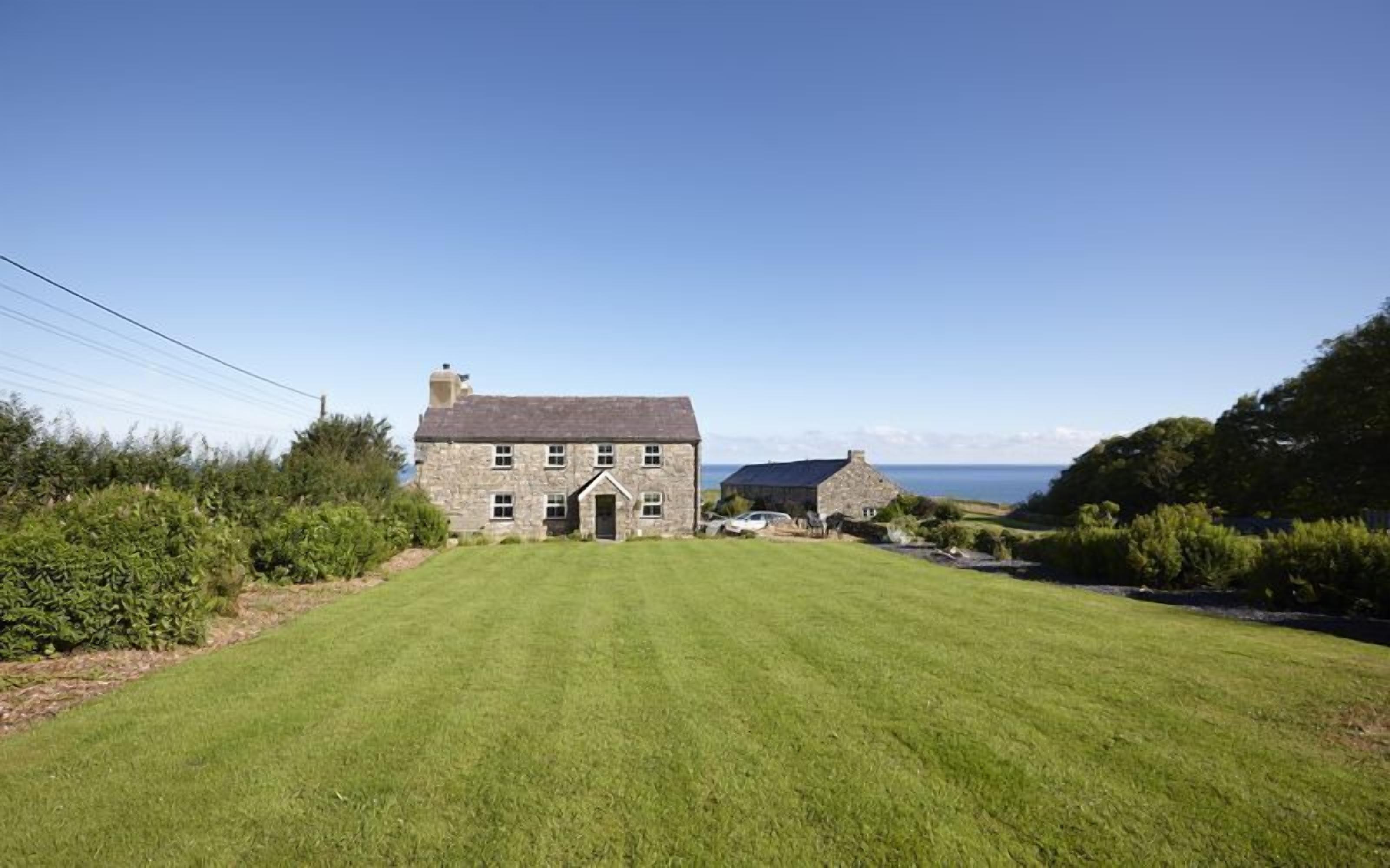 A stone house with a grassy lawn and a view of the sea.