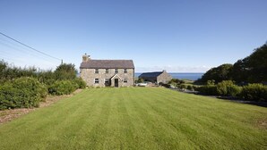 A stone house with a grassy lawn and a view of the sea.
