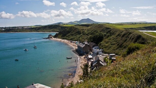 A coastal area with a beach, boats, and a mountain in the background.