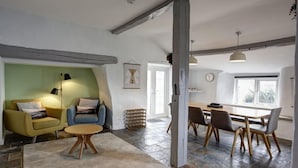 A spacious living area with a sofa, armchair, and round table, a dining area with chairs, and a large window providing natural light.