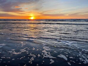A beach at sunset with waves and foam on the shore.
