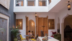 A spacious courtyard with a dining area, wooden doors, and a balcony. - Riad Lamzia (Marrakech)