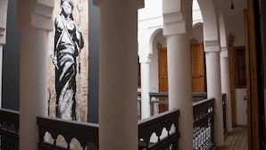A corridor with white columns, a wooden door, and a black and white mural on the wall. - Riad Lamzia (Marrakech)