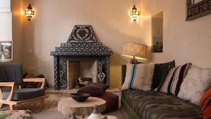 A cozy living room with a fireplace, a sofa, a chair, and a lamp. - Riad Lamzia (Marrakech)