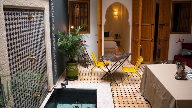 A cozy courtyard with a checkered floor, a small pool, yellow chairs, and a table with a lamp. - Riad Lamzia (Marrakech)