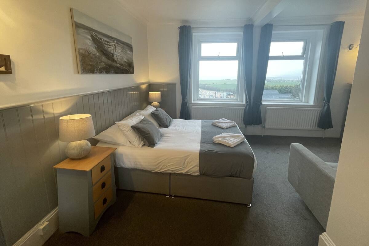 A hotel room with a bed, bedside table, lamp, and a painting on the wall.