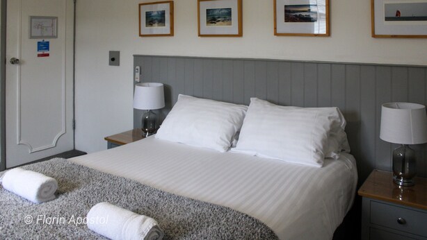 A hotel room with a neatly made bed, two bedside tables with lamps, a door with a map and sign, and three framed pictures on the wall. - The Wight Mouse Inn (Ventnor)