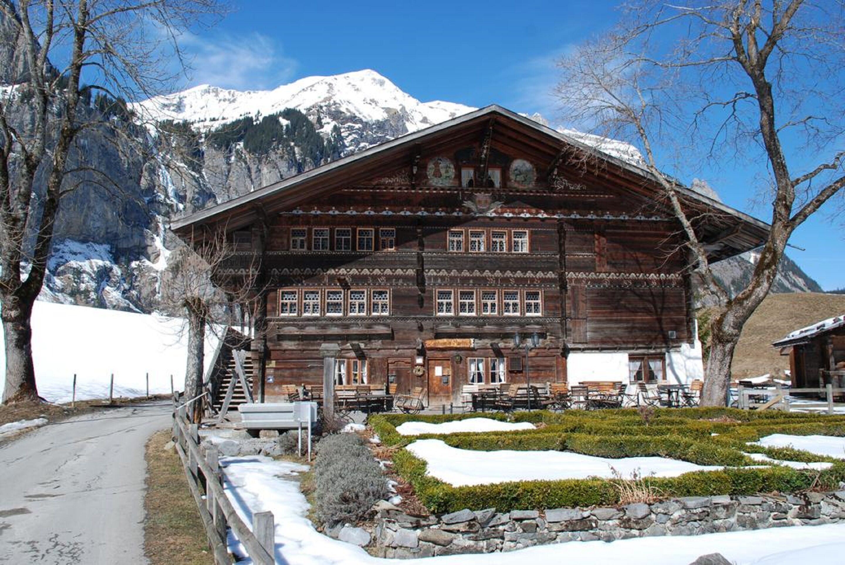 Eine Holzhütte mit schneebedecktem Dach vor einer Bergkulisse.