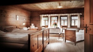 A cozy wooden cabin room with two beds, a dining table, and a window with curtains. - Landgasthof Ruedihus (Kandersteg)