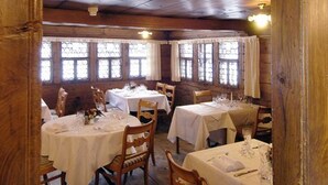 A rustic wooden dining area with tables set for dining, featuring a high ceiling and wooden beams. - Landgasthof Ruedihus (Kandersteg)