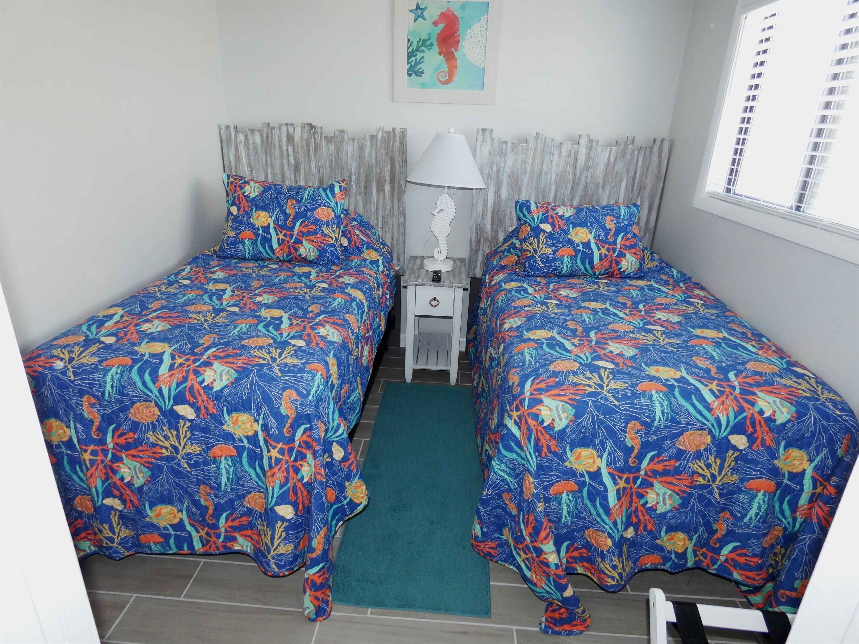 A room with two beds, a nightstand, a lamp, and a window with curtains.