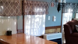 A wooden dining table with a bench, a radiator, and a couch in a room with wooden floors and patterned curtains. - Serene Mountain Resort For 2 (Gatlinburg)