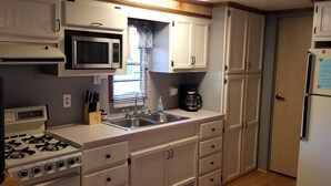 A kitchen with white cabinets, a microwave, a stove, a sink, and a refrigerator. - Serene Mountain Resort For 2 (Gatlinburg)