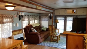 A cozy RV interior with a brown leather sofa, a small wooden table, and a kitchenette area. - Serene Mountain Resort For 2 (Gatlinburg)