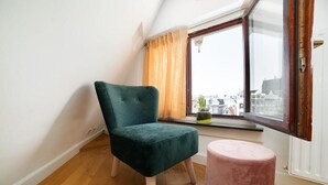 A room with a teal chair, a pink ottoman, and a window with a view of buildings. - Dase Bed & Breakfast (Amsterdam)