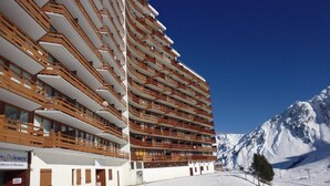 A multi-story hotel with balconies, a ski slope in the background, and a mountain range. - South-Facing Studio for 4 with Balcony, Ski-In/Ski-Out Access (La Mongie)