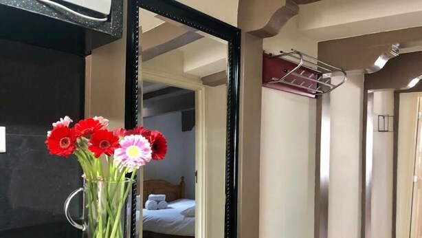 A bathroom with a large mirror, a glass vase with flowers, and a towel rack.