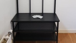A black metal shelf unit with multiple hooks and a perforated shelf.