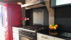 A modern kitchen with a red refrigerator, a gas stove, and a bowl of fruit on the counter.