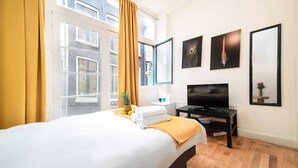 A hotel room with a bed, a TV, a desk, and a window with curtains. - Amazing B&B (Amsterdam)