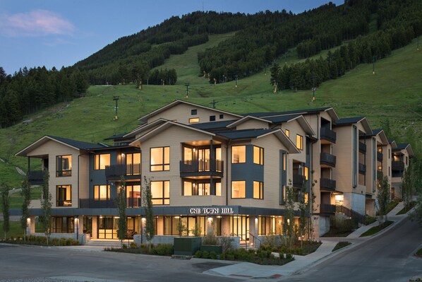 Ein mehrstöckiges Hotel mit modernem Design, gelegen an einem Hügel mit einer Skipiste im Hintergrund.