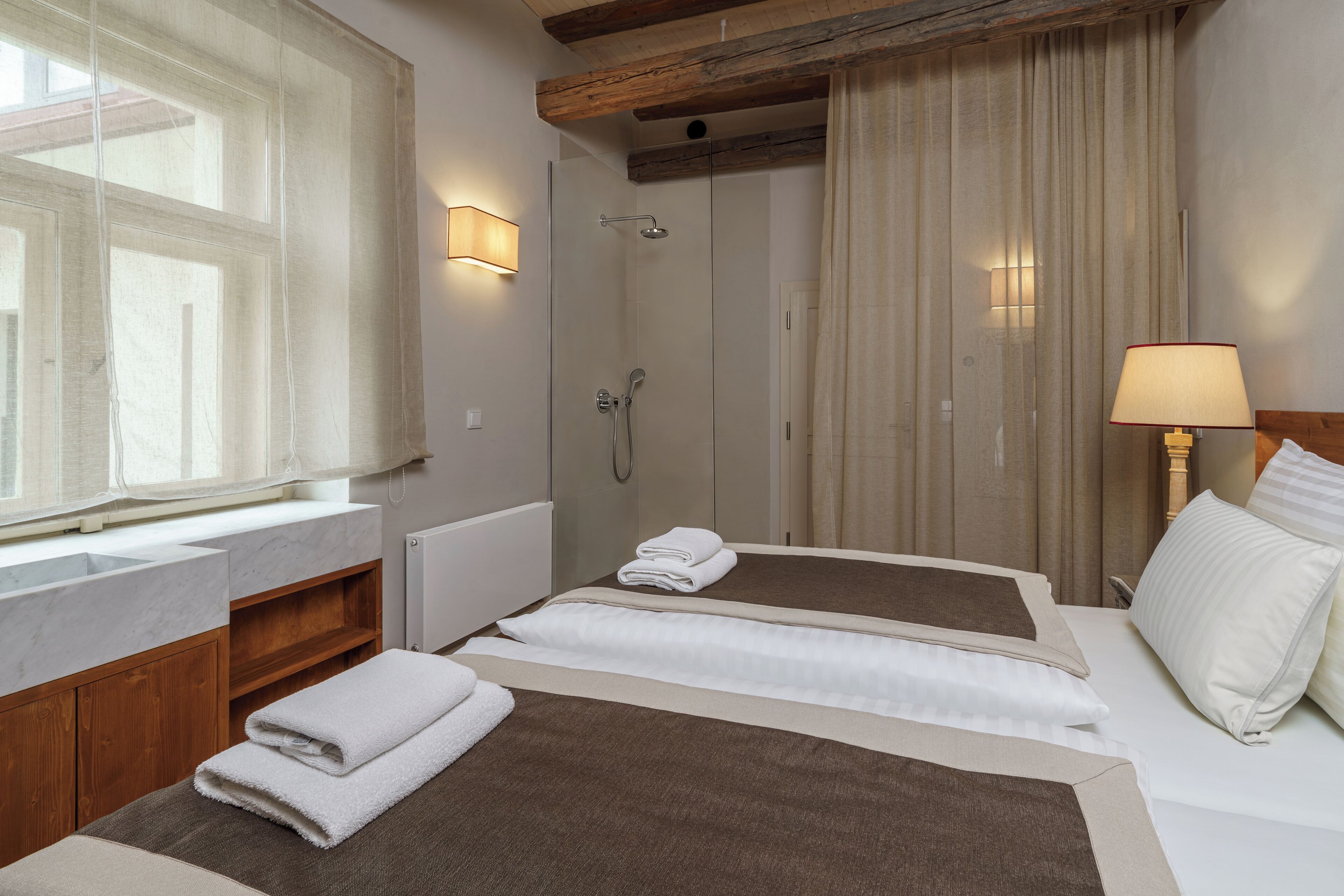 Ein Hotelzimmer mit großem Fenster, Dusche, Bett mit weißer Bettwäsche und einer Nachttischlampe.