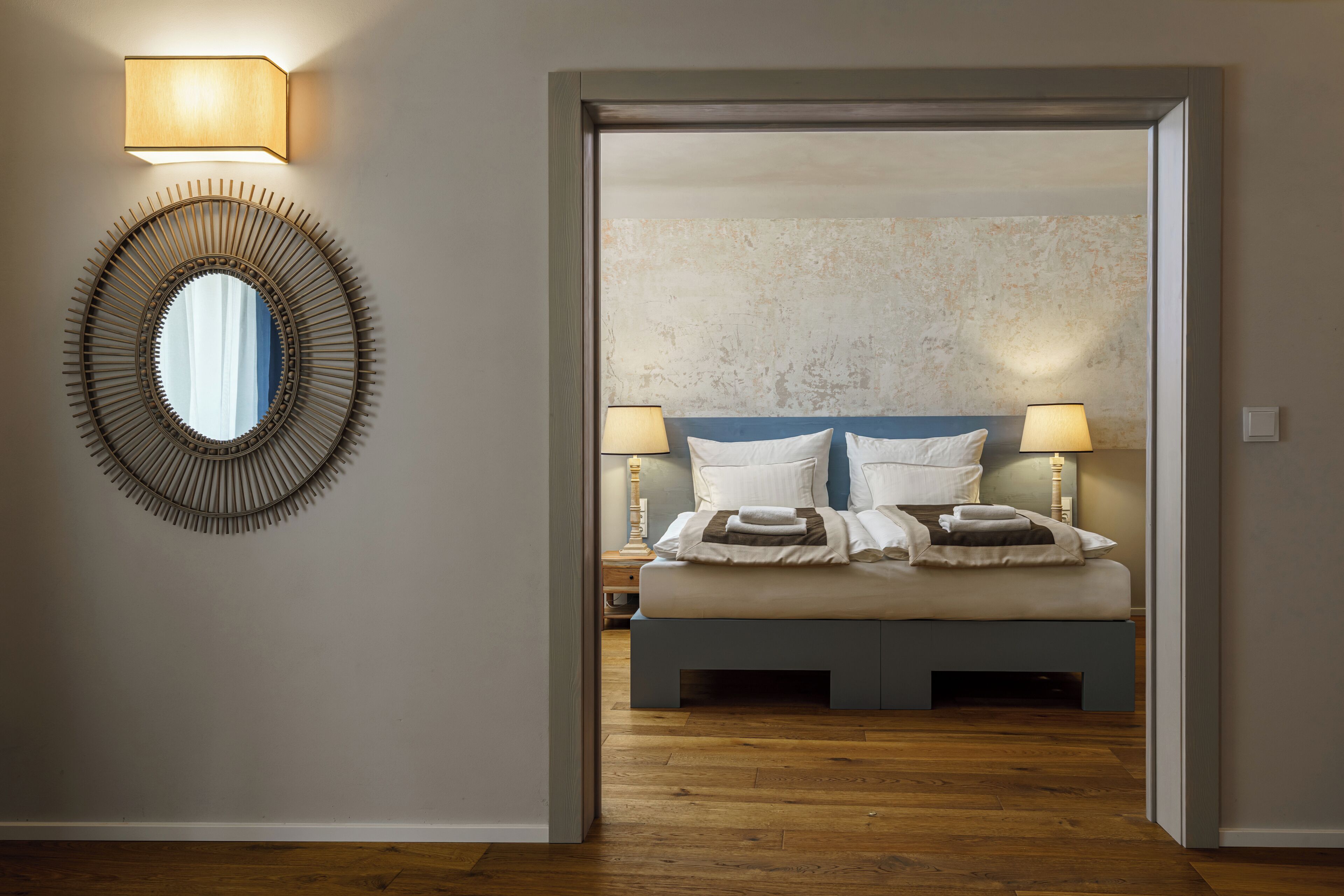 A bedroom with a bed, two bedside lamps, a round mirror, and a textured wall.