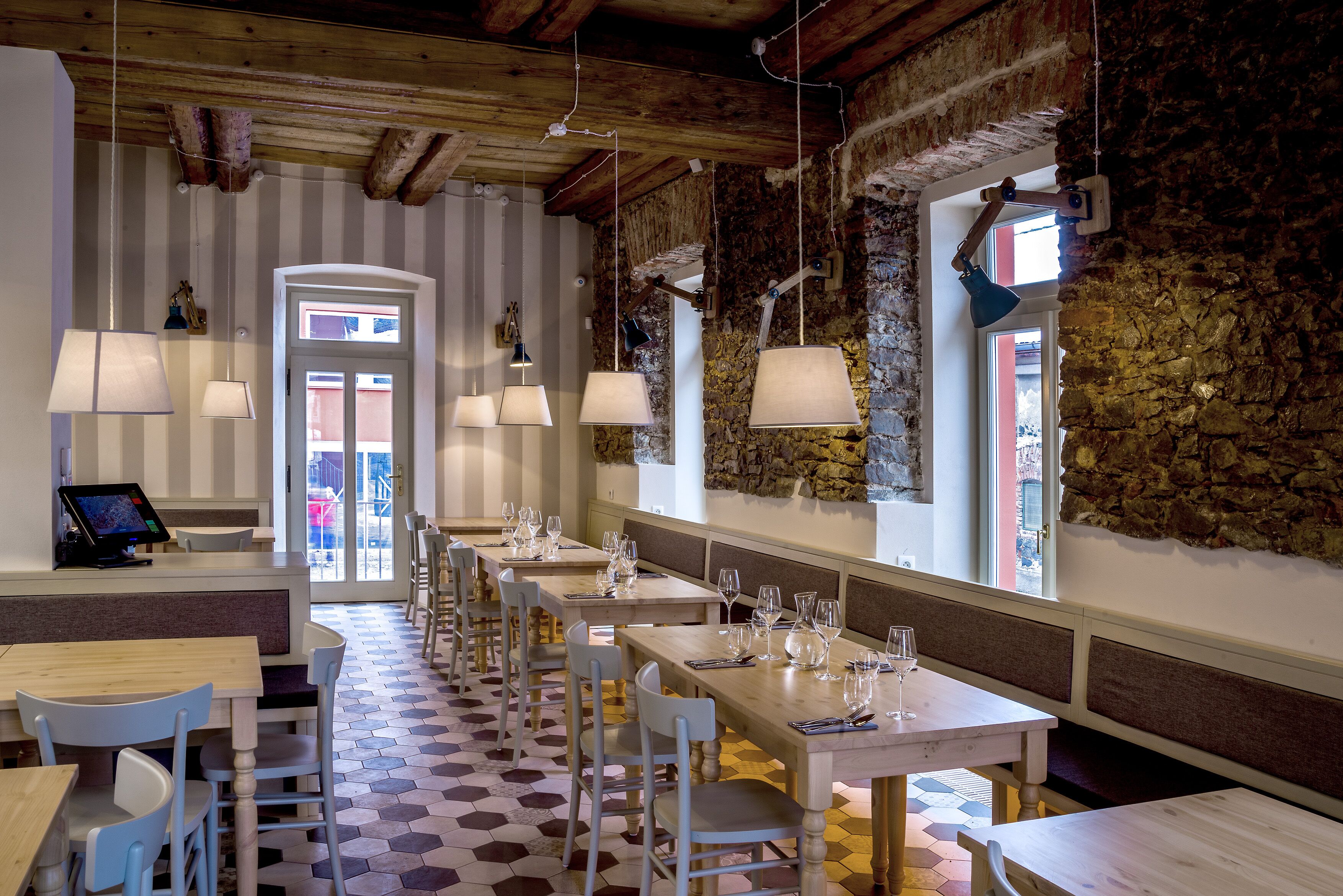Un restaurante con mesas y sillas de madera, paredes de piedra y lámparas colgantes.